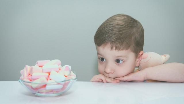 Garotinho olhando para marshmallows em cimada mesa