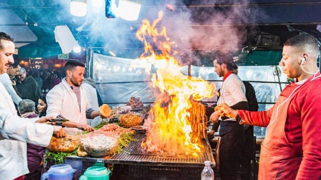 Men barbecue food as flames rise at a market stall in Marrakesh