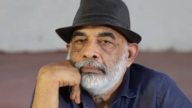 Dayapala Thiranagama wearing a hat with his head resting on his raised hand