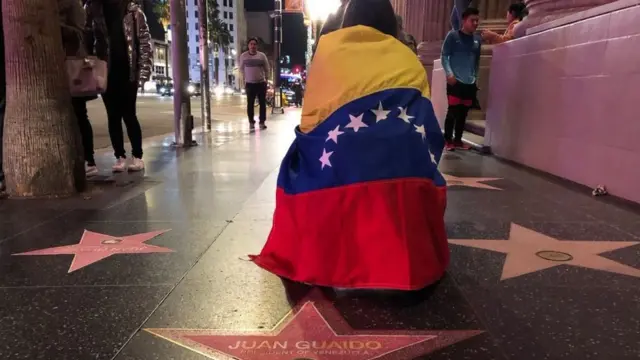 Uma mulher estájoelhos e coberta por uma bandeira venezuelana na Calçada da FamaHollywood