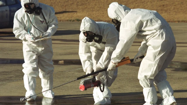 Três cientistas totalmente cobertos e com jalecos usando equipamentos na rua