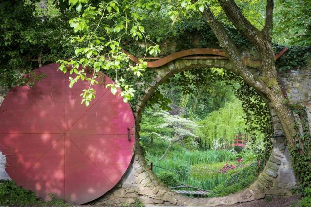 Un puerta circular tras la cual hay un jardín.