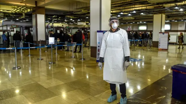 Un membre du personnel des services de santé portant un équipement de protection regarde pendant qu'il attend pour vérifier