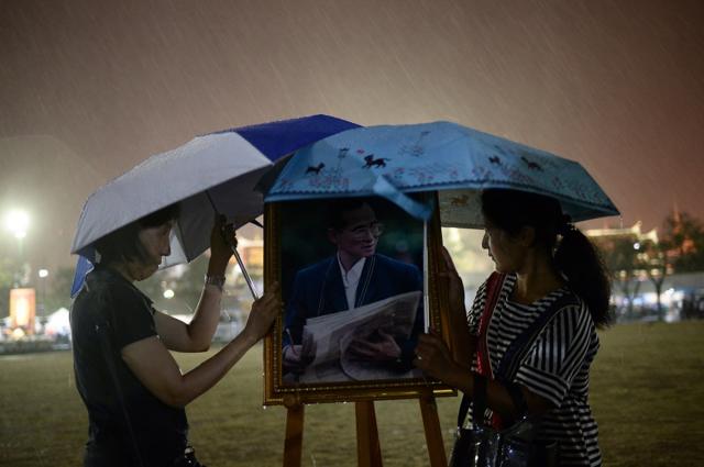Two mourners protect the picture of the late king with their umbrellas