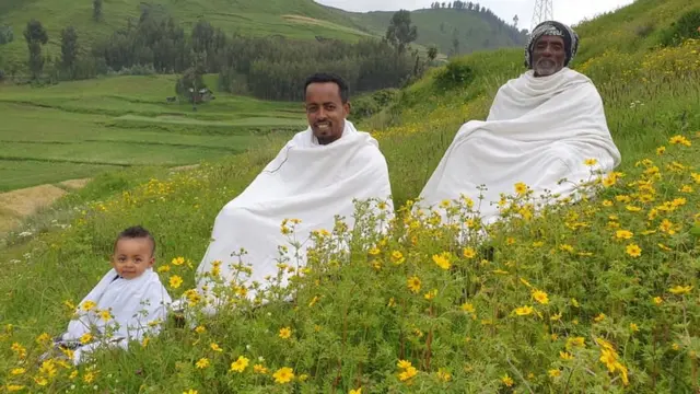 አደይ አበባ ባለበት መስክ ላይ የተቀመጡ አያት፣ አባትና ልጅ