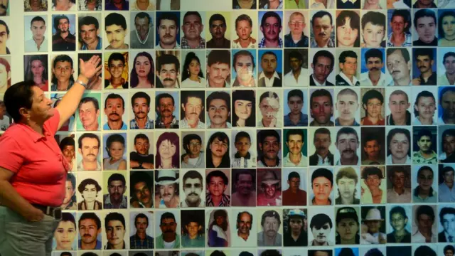 Una muer frente a un mural con fotos de víctimas del conflicto armado