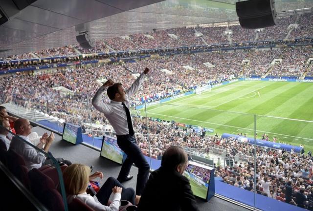Emmanuel Macron raises his arms as he watches the World Cup final in a stadium