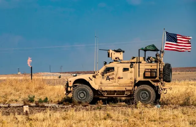 US armoured vehicle drives past a burning gas flare in north-eastern Syria