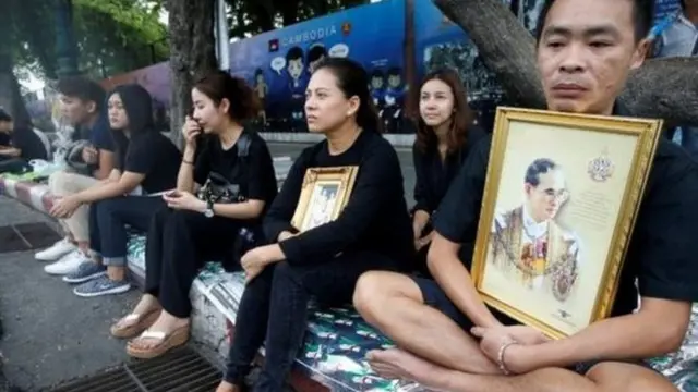 राजा की तस्वीरों के साथ शोक जाहिर करने सड़क पर बैठे लोग