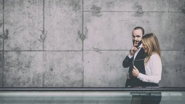 Businessman and businesswoman walking and sharing office rumors