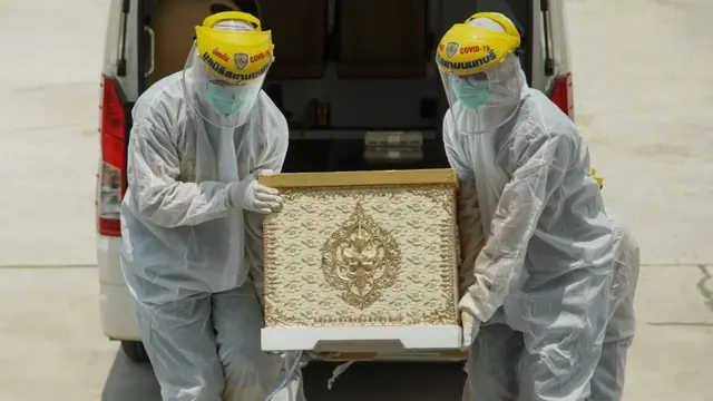 เจ้าหน้าที่สวมชุดป้องกันการติดเชื้อเคลื่อนย้ายโลงศพของผู้ป่วยโควิด-19