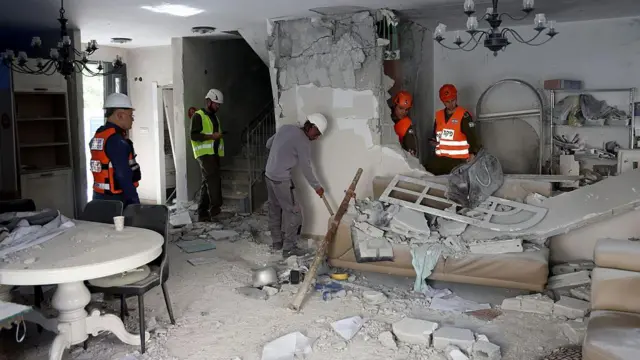 رجل إطفاء يرتدون الخوذ وثياب العمل في منزل متضرر جدرانه محطمة جراء سقوط صاروخ قرب تل أبيب