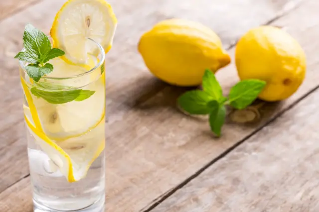 Verre d'eau citronnée avec menthe et deux citrons sur la table.