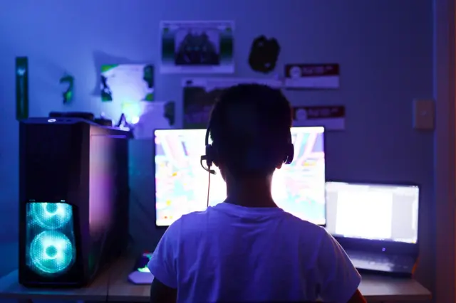 Menino em frente a um computador, usando headphones