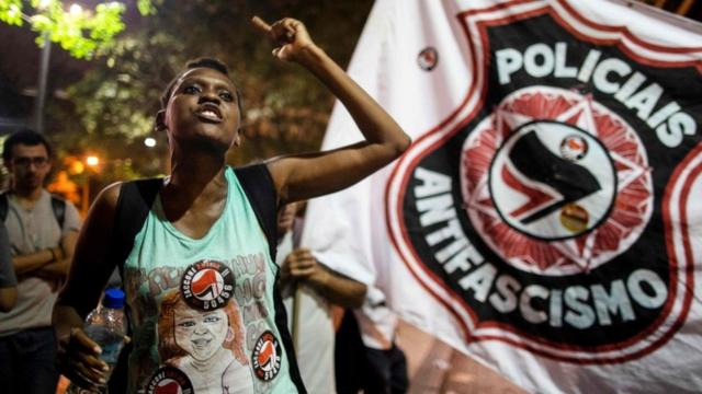 Manifestante com cartaz atrás dizendo "policiais antifascismo" em protesto contra Bolsonaro