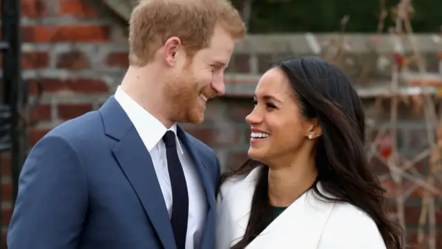 Príncipe Harry e Meghan Markle olhando um para o outro e sorrindo