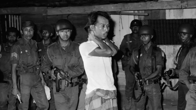 A suspected sympathizer with the Communist-led abortive coup of October 1th is questioned under gunpoint. The Indonesian Army is continuing its careful screening in an effort to uproot dissenters.