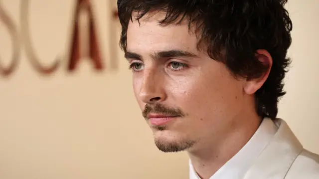 Тимоти Шаламе у белом оделу гледа са стране