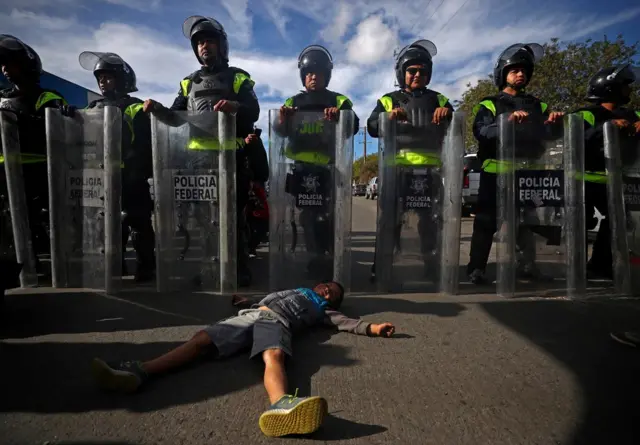 A six-year-old migrant boy lies on the floor in front of Mexican riot police