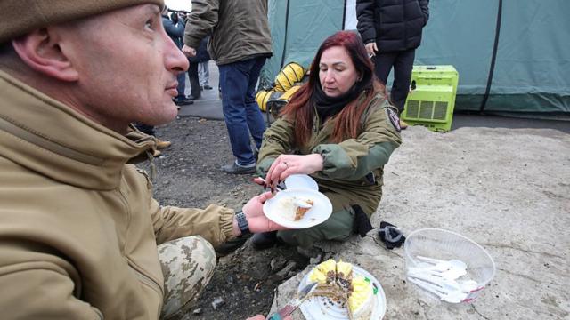 женщина кладет бывшему украинскому пленному кусок пирога