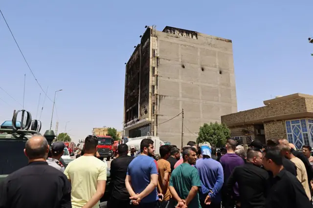 تجمّع مواطنون عراقيون في 17 يوليو/تموز 2025 أمام مبنى متفحم، عقب اندلاع حريق ليلي في مركز "هايبر مول" التجاري حديث الافتتاح، وسط مدينة الكوت شرقي العراق.

