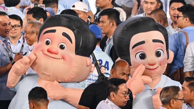 People walk past mascots‌ depicting presidential candidate and Indonesia's⁢ Defence Minister Prabowo Subianto (L) and vice presidential candidate Gibran Rakabuming Raka (R)