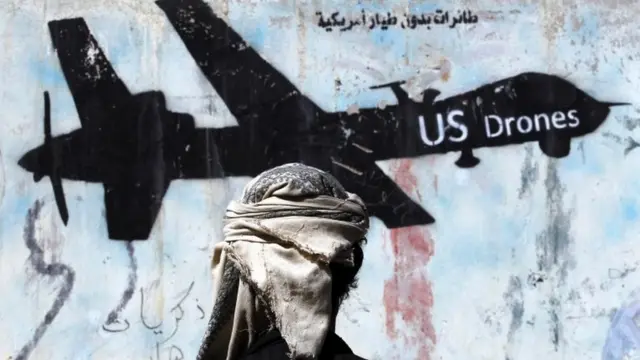 যুদ্ধ বিধ্বস্ত ইয়েমেনে আমেরিকান সামরিক তৎপরতার বিরুদ্ধে এক দেয়াল লিখনের সামনে দাঁড়ানো একজন ইয়েমেনী