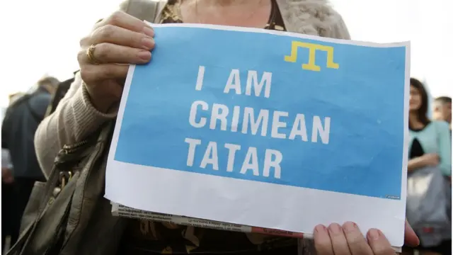 Жінка тримає плакат з написом "Я - кримська татарка" англійською