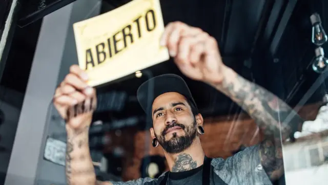Joven latino abriendo colgando el cartel de abierto en un restaurante.