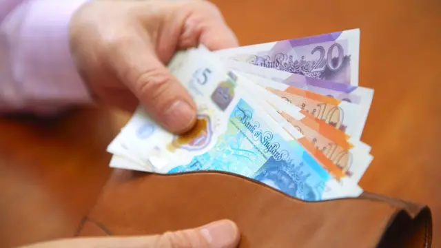 Una mano guardando billetes de libras en una billetera