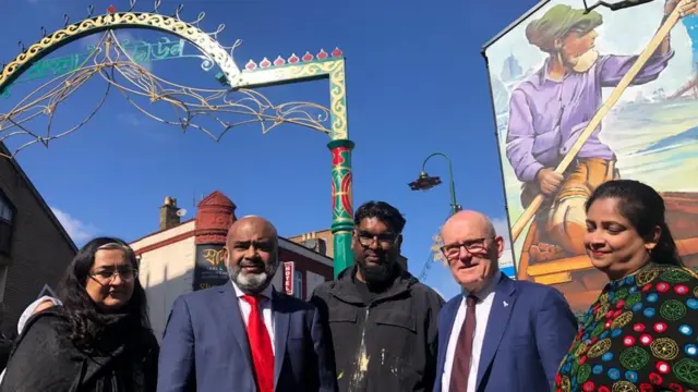 ম্যুরালের উদ্বোধনী আয়োজনে শিল্পীর সাথে মেয়র জন বিগস (ডান থেকে দ্বিতীয়)। পাশে টাওয়ার হ্যামলেটস কাউন্সিলের অন্যান্য কর্মকর্তা।