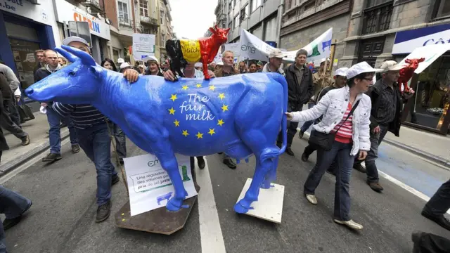 Manifestantes marchan arrastrando una vaca pintada con los colores de la UE encima de la cual hay otra más pequeña con los colores de la bandera belga
