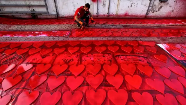 伊拉克库尔德人在埃尔比勒街头为情人节庆祝做准备，他用油漆喷枪为心形图案上红色。