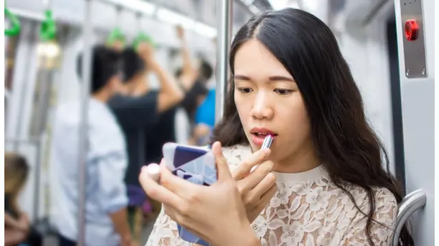 Mulher passa maquiagem no trem