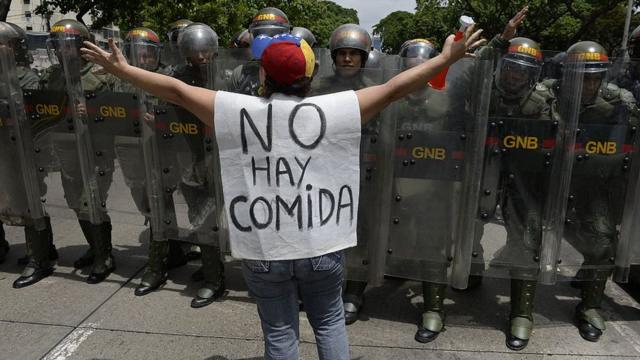 Mujer con un chaleco que dice: "No hay comida", parada frente a policías venezolanos.