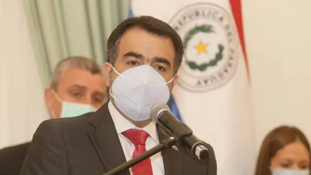 Ministro fala no microfone, de máscara