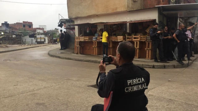 Peritos na rua São Daniel fotografando a torre branca ao fundo da favela