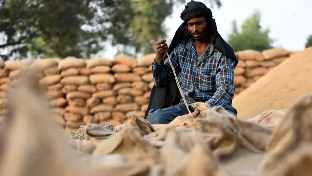 ਅਨਾਜ ਦੀਆਂ ਬੋਰੀਆਂ ਉੱਪਰ ਬੈਠਾ ਮਜ਼ਦੂਰ