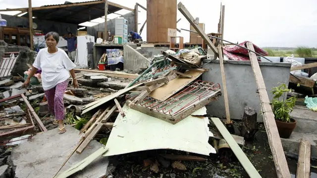 A woman walks in the ruins of her house