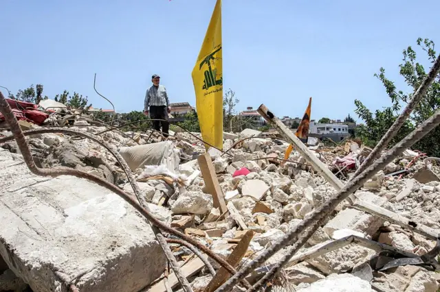 Una bandera amarilla de Hezbolá se erige de los escombros de lo que pudo ser un edificio.