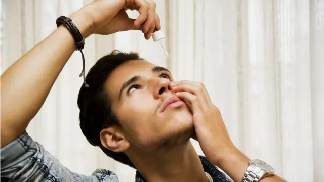 Hombre joven echándose gotas en los ojos.