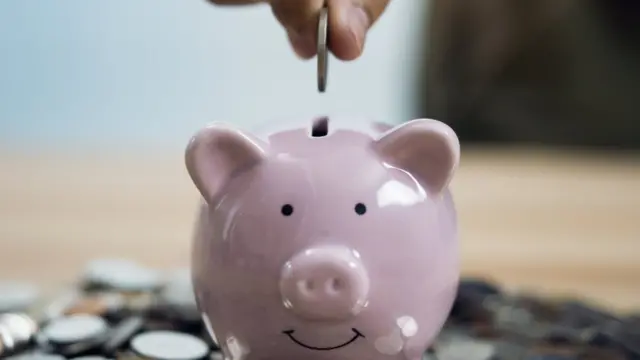 Mano depositando monedas en una alcancía.