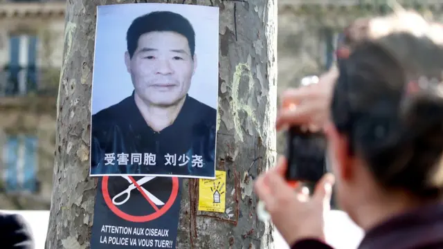巴黎共和国广场悼念刘少尧集会现场一名男子朝着贴在树上的刘少尧遗照拍照（2/4/2017）