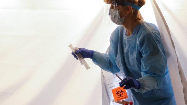 Nurse Becky Barton walks out of a tent with a test kit at a drive-through testing site for coronavirus, flu and RSV, currently by appointment for employees at UW Medical Center Northwest in Seattle, Washington, U.S. March 9, 2020