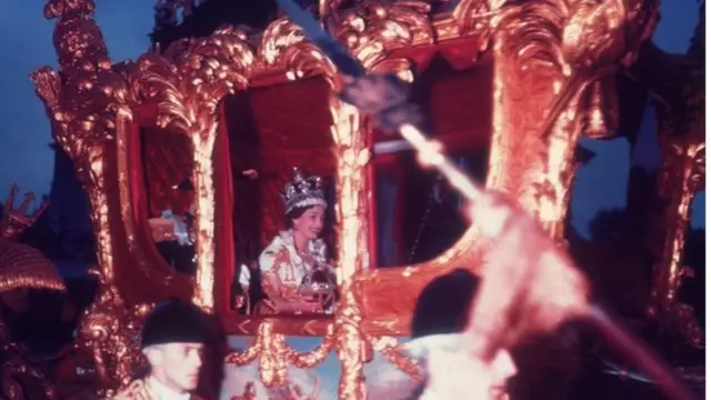 Foto colorida mostra a rainha Elizabeth jovem, usando a coroa real, em uma carruagem dourada
