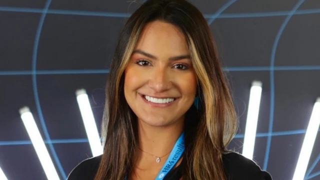 Gabriela Xavier sorrindo para foto em frente a painel iluminado; ela usa um crachá