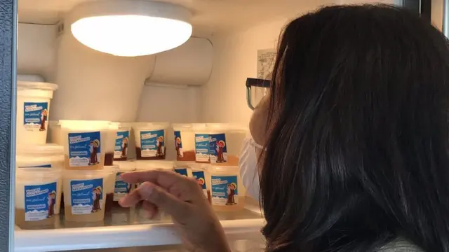 Una mujer frente a envases de yogurt en una refrigeradora.