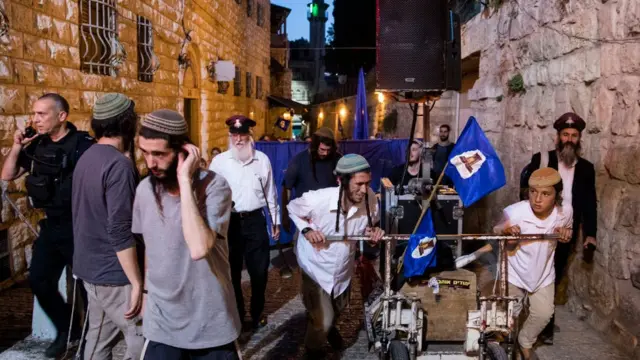 يحمل المشاركون في المسيرة مكبرات صوت عملاقة لبث الأغاني القومية الإسرائيلية وهم يسيرون عبر أزقة البلدة القديمة
