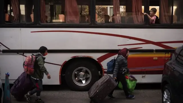 Peruanos varados en Chile caminando con sus valijas frente a un autobús