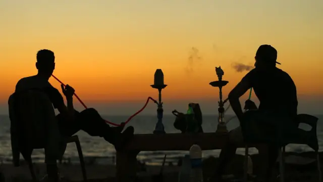 Shadow of two young men wey dey smoke shisha inside beach.